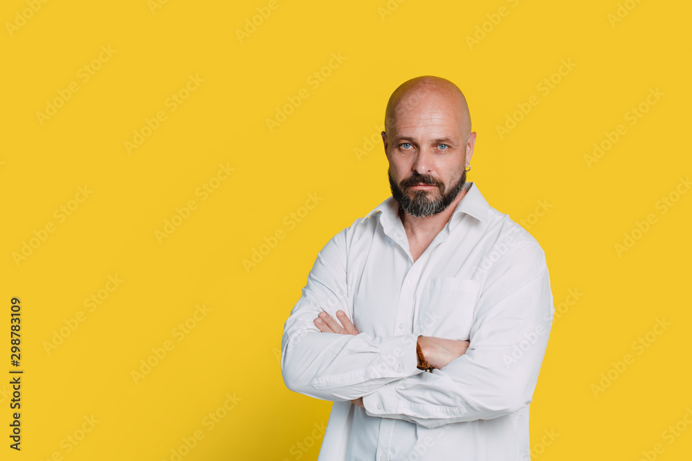 Serious middle-aged man with folded arms and a deadpan expression posing in front of a yellow background with copy space Serious middle-aged man with folded arms and a deadpan expression posing in front of a yellow background with copy space
