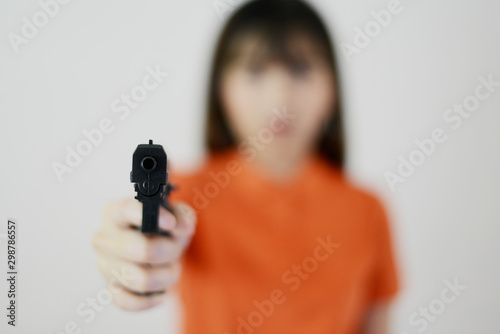 Woman with orange shirt is holding black gun on white isolated background