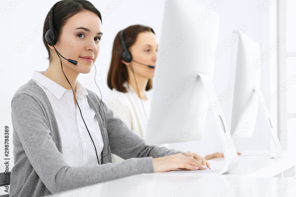 Call center. Beautiful woman receptionist sitting in headset at customer service office. Group of operators at work. Business concept Call center. Beautiful woman receptionist sitting in headset at customer service office. Group of operators at work. Business concept