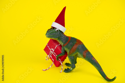 funny green dinosaur toy in little santa claus hat with red gift box  on vibrant yellow background photo