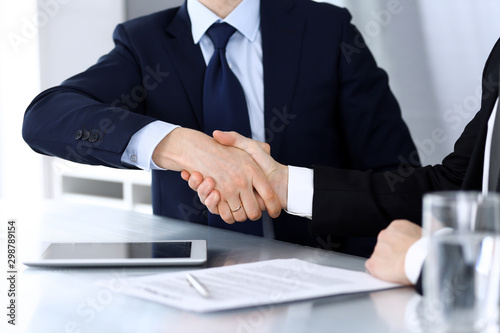 Business people shaking hands after contract signing in modern office. Unknown businessman with colleagues at meeting or negotiation. Teamwork, partnership and handshake concept