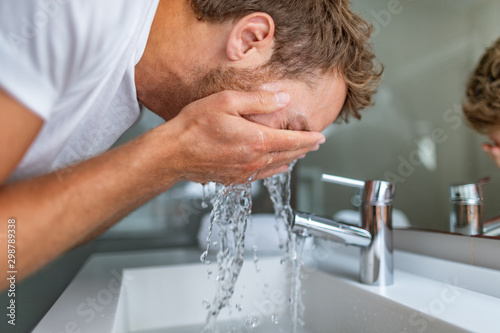 Face wash man in bathroom washing cleansing for acne facial treatment in sink splashing cold water onto face. Men beauty skincare lifestyle.