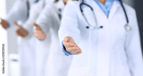 Group of modern doctors standing as a team whole offering helping hand for shaking hand or saving life. Physicians ready to examine and help patients in hospital office. Medical help, insurance in