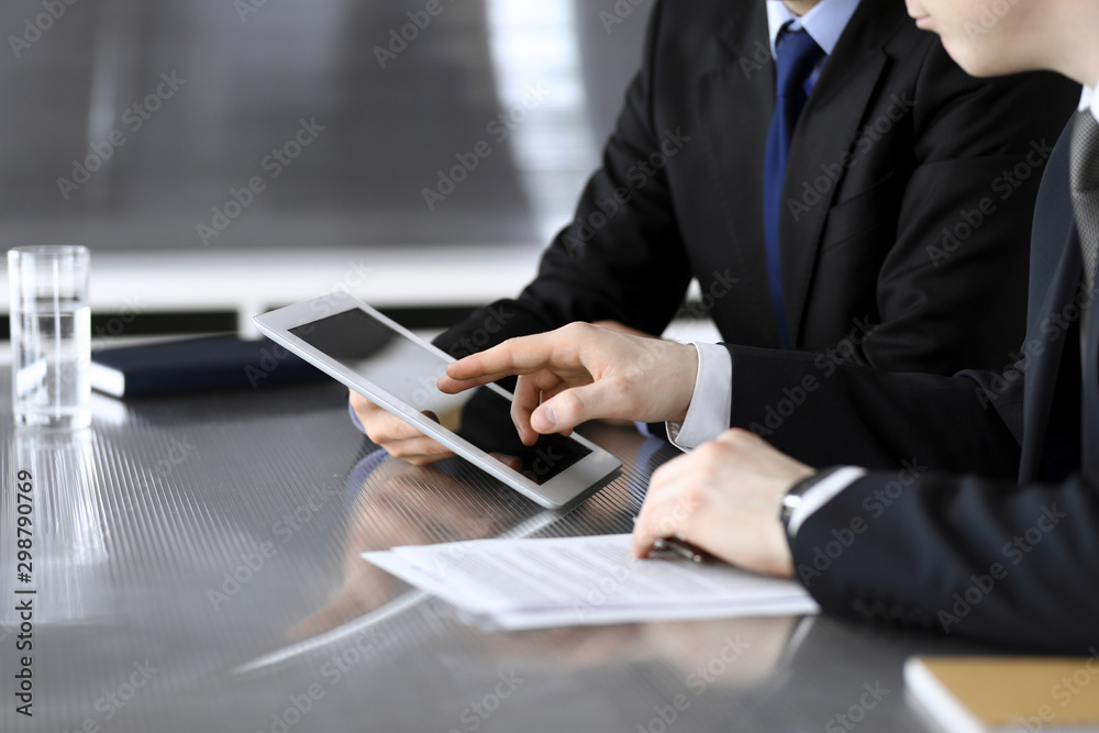 Businessman using tablet computer and work together with his colleague or partner at the glass desk in modern office, close-up. Unknown business people at meeting. Teamwork and partnership concept Businessman using tablet computer and work together with his colleague or partner at the glass desk in modern office, close-up. Unknown business people at meeting. Teamwork and partnership concept