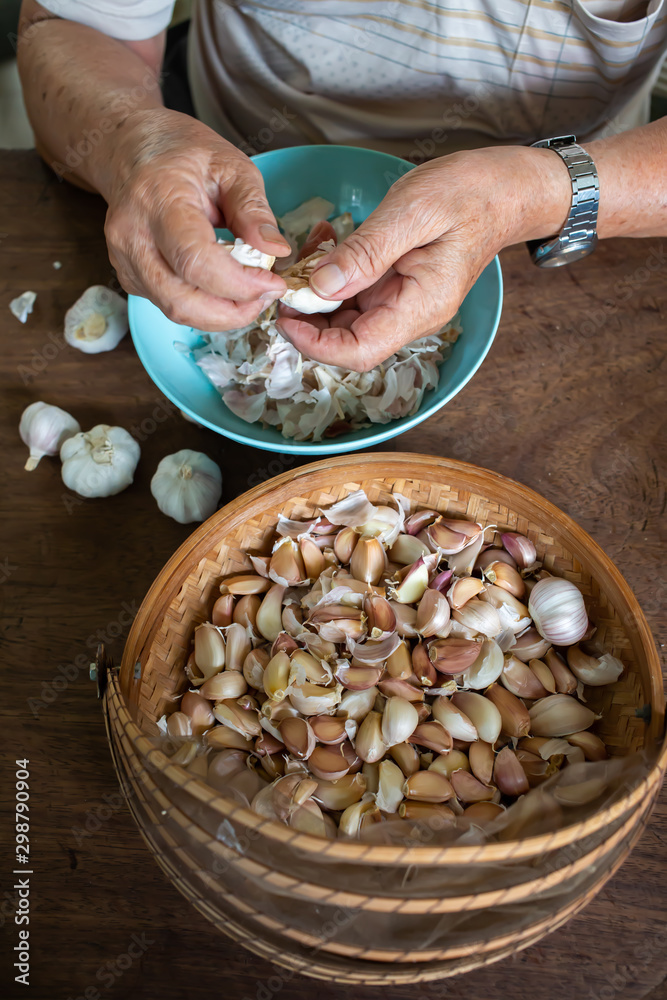 Senior man's hands peeling Garlic or Allium sativum on wood background, Kitchen Process concept