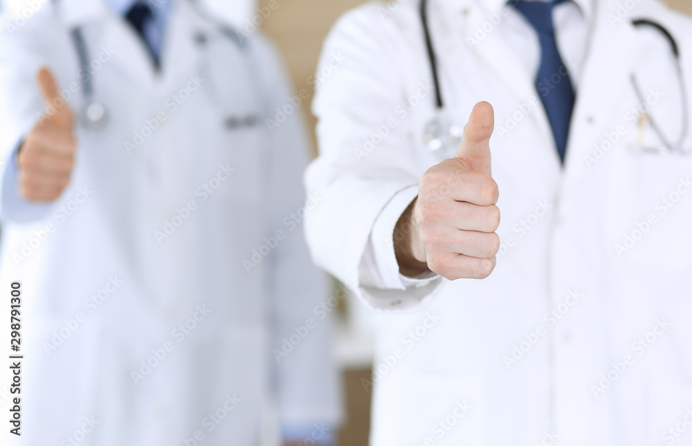 Group of modern doctors standing as a team with thumbs up or Ok sign in hospital office, close-up. Physicians ready to examine and help patients. Medical help, insurance in health care, best treatment Group of modern doctors standing as a team with thumbs up or Ok sign in hospital office, close-up. Physicians ready to examine and help patients. Medical help, insurance in health care, best treatment