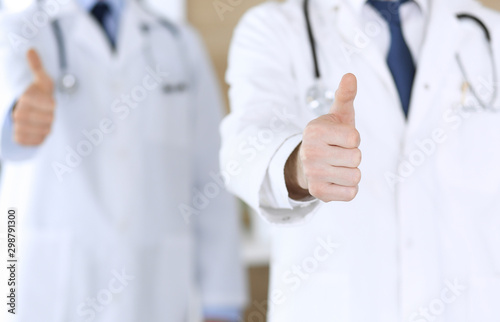 Group of modern doctors standing as a team with thumbs up or Ok sign in hospital office, close-up. Physicians ready to examine and help patients. Medical help, insurance in health care, best treatment