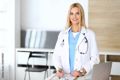 Doctor woman at work in hospital excited and happy of her profession. Blonde physician controls medication history records and exam results. Medicine and healthcare concept