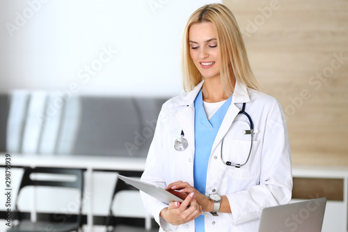 Doctor woman at work in hospital excited and happy of her profession. Blonde physician controls medication history records and exam results while using tablet computer. Medicine and healthcare concept