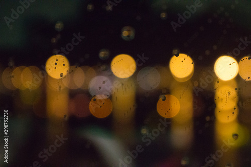 Blurred city lights with rain drops foreground. Unfocused colorful lights behind glass with drops. Shiny lights of night bokeh. Unfocused bright colors background.