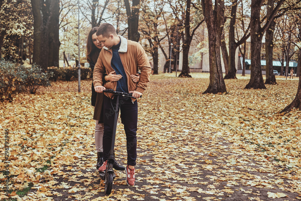 Attractive couple has a nice romantic walk at autumn park with scooter. Attractive couple has a nice romantic walk at autumn park with scooter.
