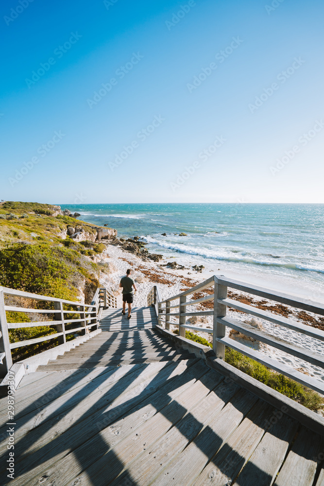 Man walking down a staircase to Burns beach, Perth Western Australia. On a bright sunny day, with perfect beach weather.