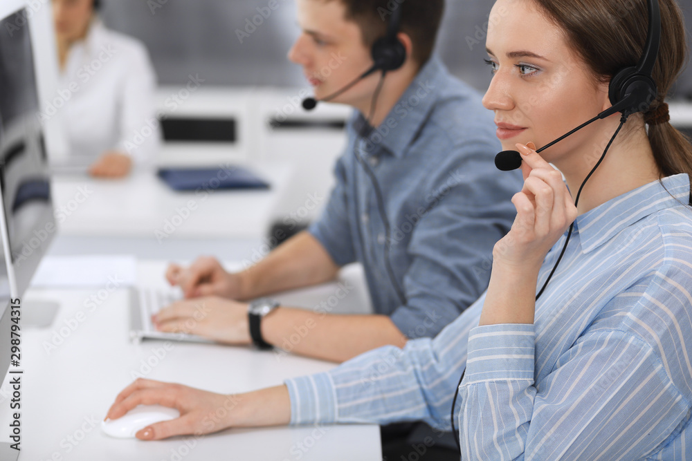 Call center. Group of casual dressed operators at work. Focus on business woman in headset at customer service office. Telesales in business Call center. Group of casual dressed operators at work. Focus on business woman in headset at customer service office. Telesales in business