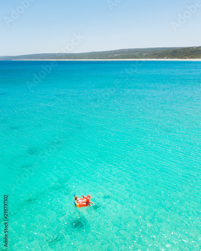 Young woman floating away on a parrot inflatable in the stunning light blue water at Hamelin Bay, Western Australia.