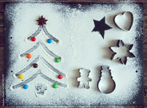 Christmas cooking. Xmas tree with decorations and candies made from flour on a dark table, ingredients for baking on dark background, top view photo