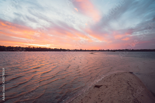 Stunning array of colours at sunset over the river ripples and sand bank at Point Walter, Perth, Western Australia with Perth City as the background.