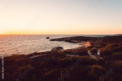 Lone woman at sunset walking down a path towards the beach lit up by orange light at Point Peron  Rockingham  Perth  Western Australia.