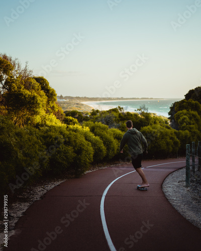 Lone skater, skating through the beach shrubs down the path at Mullaloo beach lookout towards the beautiful ocean and beach.  photo