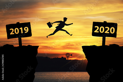 Businessman jumping between 2019 and 2020 years with sunset background