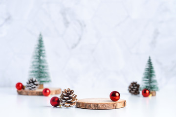 christmas tree with pine cone and decor xmas ball and empty wood log plate on white table and marble tile wall background.clean minimal simple style.holiday still life mockup to display design