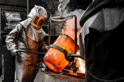 In a foundry workshop. A worker protected by a safety suit pours the molten metal into a mold photo