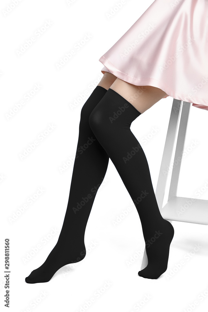 Fotka „Medium bottom shot of female legs in black shadow-proof stockings  with closely rims on the top. The girl in a pink satin skirt is sitting on  the white bar stool on