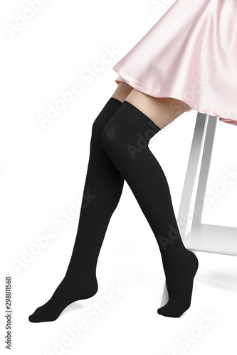 Medium bottom shot of female legs in black shadow-proof stockings with closely rims on the top. The girl in a pink satin skirt is sitting on the white bar stool on the white background. photo