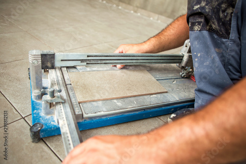 A construction worker cuts a ceramic tile using a tile cutting machine.