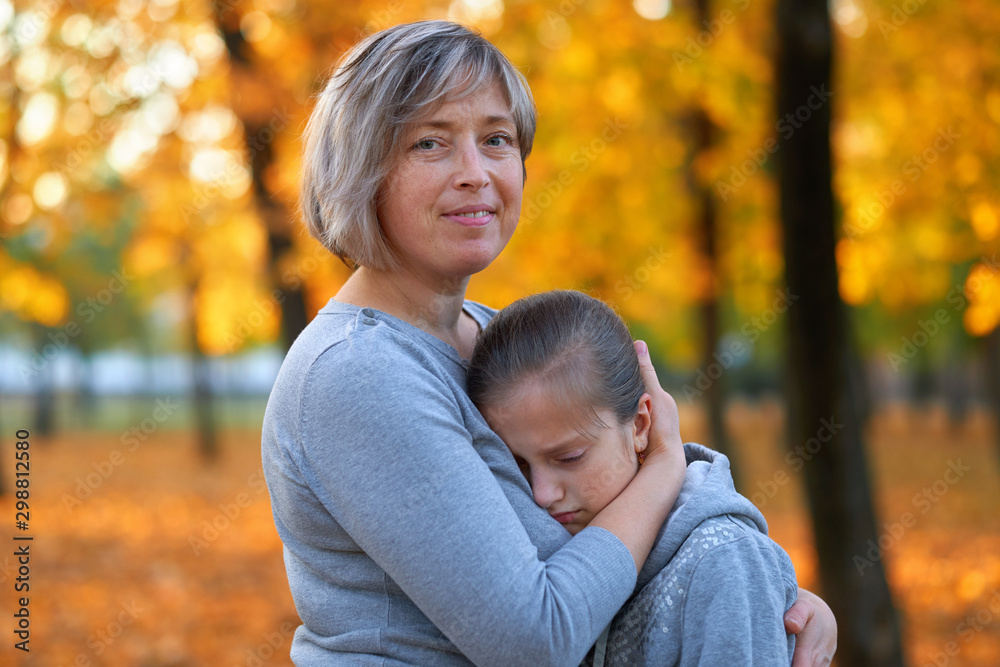 Portrait of mother with her sad daughter in autumn city park. Bright yellow trees and leaves