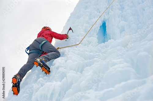 Alpinist woman with ice tools axe in orange helmet climbing a large wall of ice. Outdoor Sports Portrait.