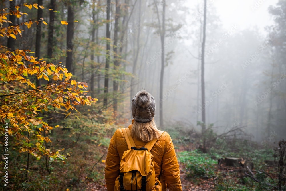 Woman with knit hat and backpack hiking in foggy woodland
