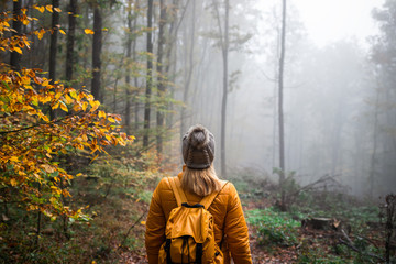 Woman with knit hat and backpack hiking in foggy woodland