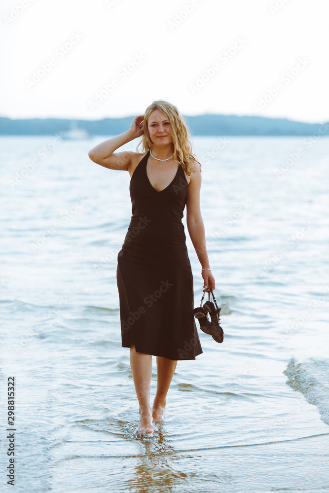 woman in black light dress walking barefoot by sea beach Stock Photo ...