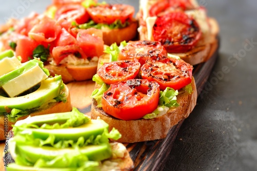 Bruschetta on a dark table background. Bruschetta with tomatoes, mozzarella and avocado. Delicious vegetarian healthy sandwiches. Tasty snack on the pink plate.