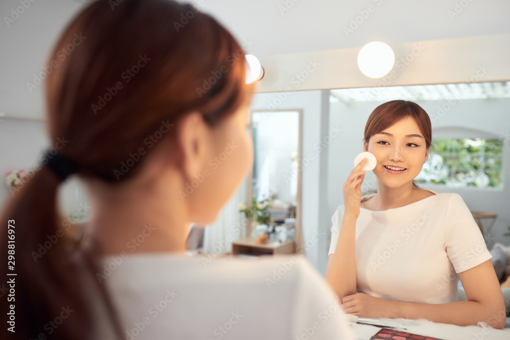Young Asian woman cleaning her face in front of mirror Young Asian woman cleaning her face in front of mirror