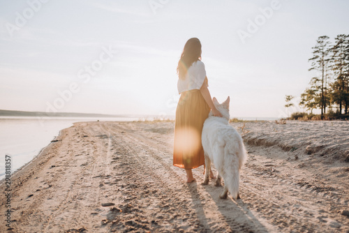 A girl walks with a white Swiss shepherd by the lake