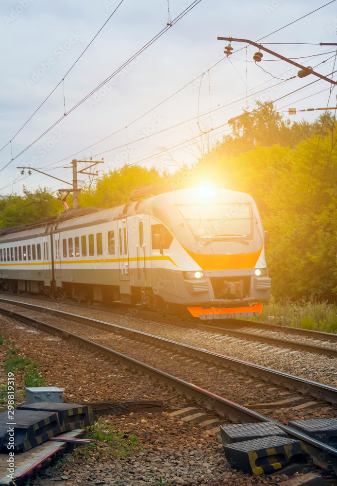 Naklejka premium commuter train rides on railway tracks in city with green trees in background