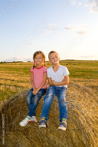 happy children sitting on haystack at sunset. kids, girl with boy sitting in field