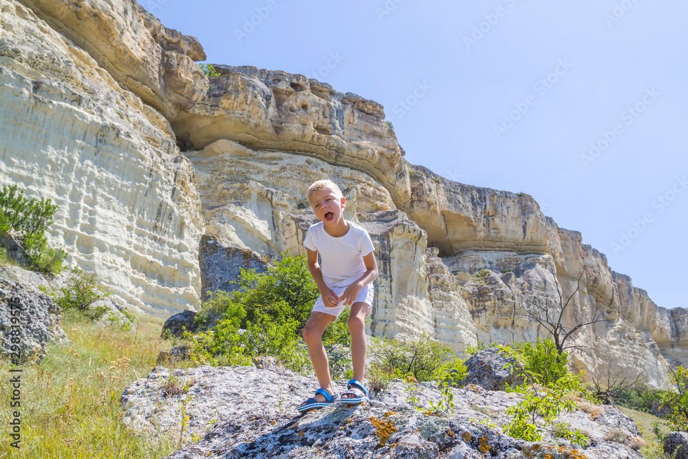 little boy stands on rock in the mountains and growls like a dinosaur or a zombie
