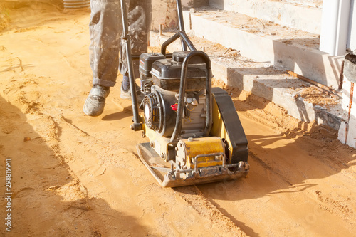 worker compresses sand in blind area around building with special working tool (tamping machine) photo