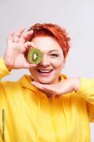 edhead woman in yellow hoodie covering eye with kiwi fruit photo