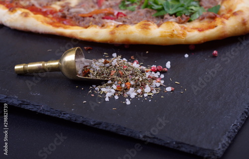 a silver scoop with coarse salt and seasonings lies fuss pizza on a dark background photo