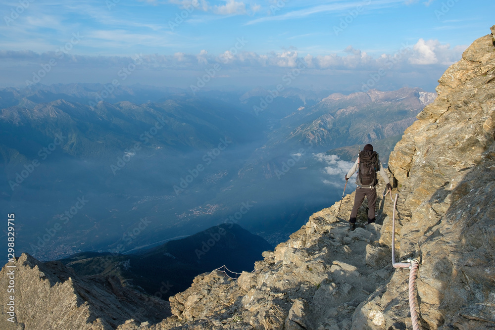 Hiker on the steep and exposed path over the ridge to the summit of Rocciamelone in the Italian Alps
