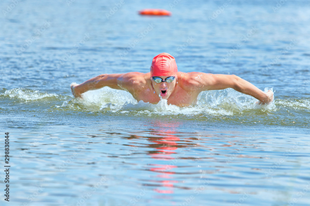 dynamic and fit swimmer in cap and goggles, breathing performing the butterfly stroke in water