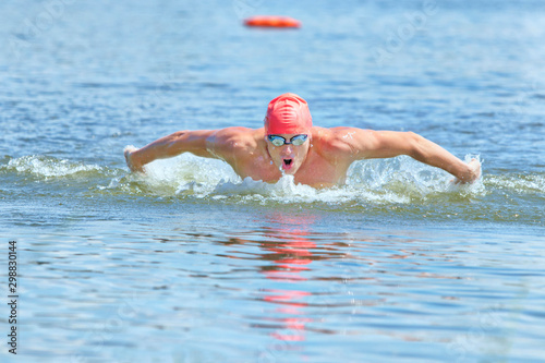 dynamic and fit swimmer in cap and goggles, breathing performing the butterfly stroke in water