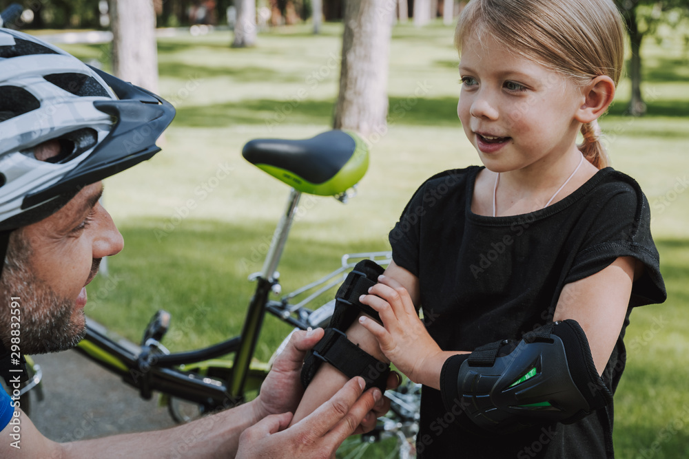 Obraz premium Young man in protective helmet helping daughter to put on elbow pads