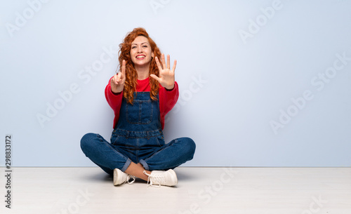 Redhead woman with overalls sitting on the floor counting six with fingers