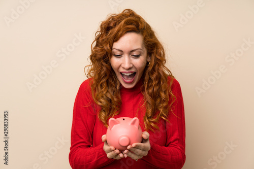 Redhead woman with turtleneck sweater holding a big piggybank