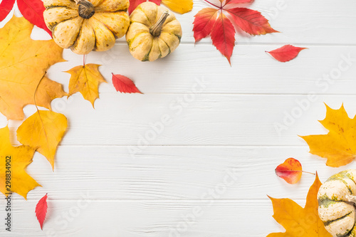 Autumn flat lay. Pumpkins and yellow leaves on white wooden background. Space for text.