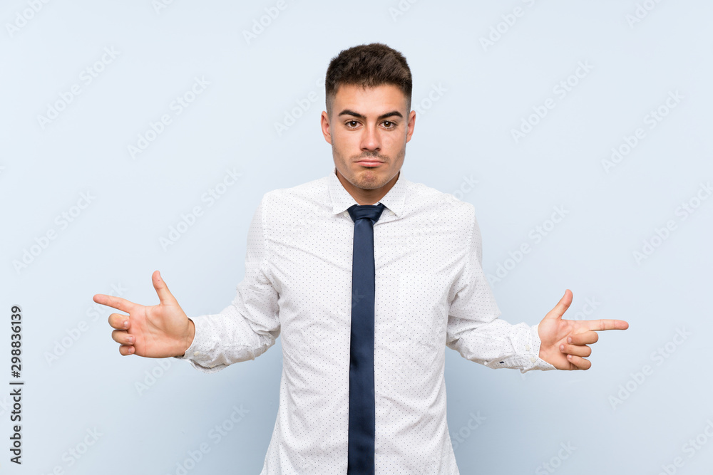Handsome businessman over isolated blue background pointing to the laterals having doubts Handsome businessman over isolated blue background pointing to the laterals having doubts